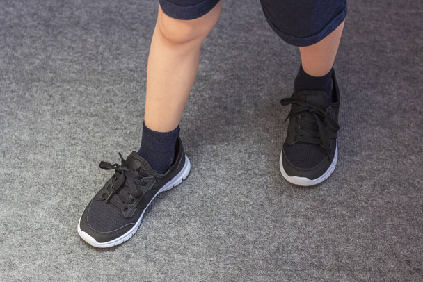 Young boy's legs in textile fashion black sneakers. Children's trendy casual outfit and street fashion. Top view, Close up, toned - Foto, Imagem