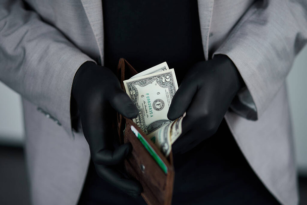 黒い医療用手袋を手に金を持って財布を持っている男。コロナウイルスの危機。金を貯めろ。お金はない。世界危機 - 写真・画像