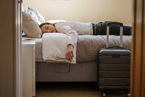 Tired businesswoman is sleeping dressed in hotel room. - Zdjęcie, obraz