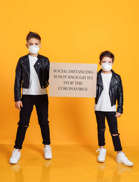Koronawirus Covid-19. Dwóch chłopców w maskach ochronnych i trzymających znak "Odległość społeczna" to za mało, by powstrzymać Koronawirusa. - Zdjęcie, obraz