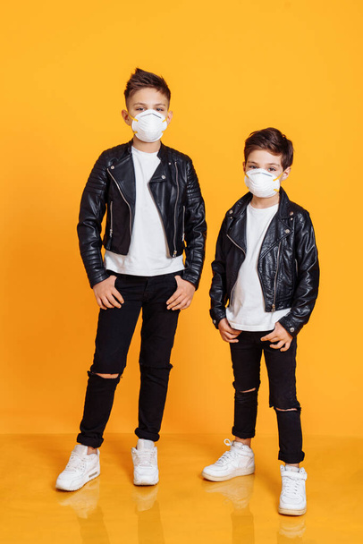Porträt europäischer Kinder mit medizinischer Maske im gelben Studio. Konzept der Coronavirus-Quarantäne oder Covid-19. Die Maske Atemschutz  - Foto, Bild