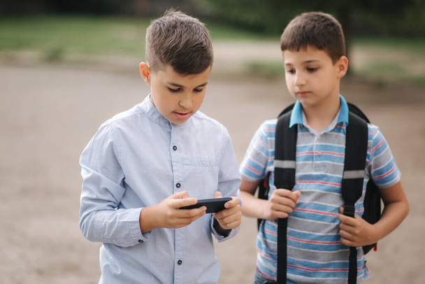Два мальчика играют в онлайн-игры в карантине. Мальчики улыбаются и пользуются телефоном - Фото, изображение