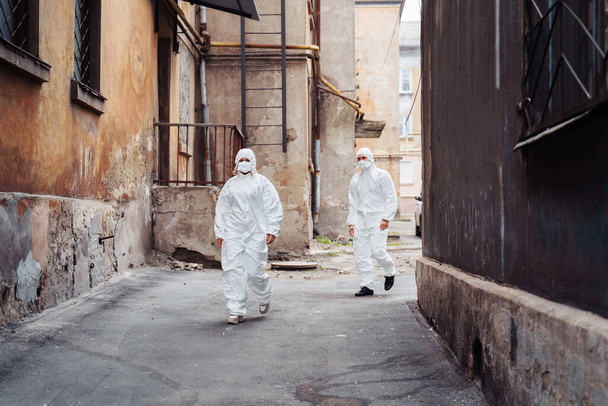 Άνθρωποι με προστατευτικές στολές και αναπνευστήρες περπατούν έξω κατά μήκος εγκαταλελειμμένων, εγκαταλελειμμένων, κατεστραμμένων δρόμων κατά τη διάρκεια του πολέμου. Έννοια του Coronavirus. - Φωτογραφία, εικόνα