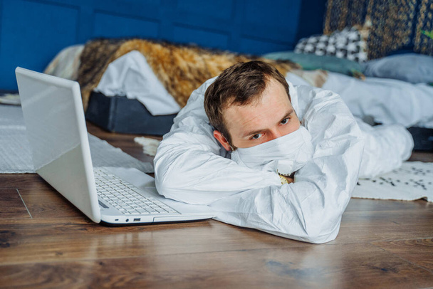 Smutny pacjent leżący na podłodze w domu z laptopem z powodu epidemii koronawirusa. Portret zaniepokojonego, zmęczonego i zaniepokojonego lekarza badającego statystyki pandemii covid-19. - Zdjęcie, obraz