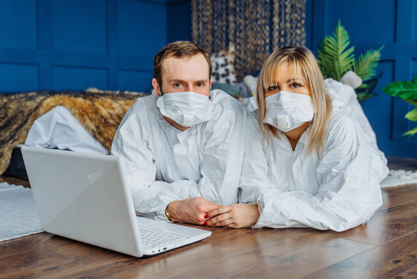 Να προσέχεις και μείνε σπίτι! Γιατροί ξαπλωμένοι στο πάτωμα φορώντας μάσκες προσώπου κατά του ιού της στέψης. Άτομα με προστατευτικές στολές που απομονώθηκαν λόγω επιδημίας covid-19 και εργάζονται σε laptop - Φωτογραφία, εικόνα