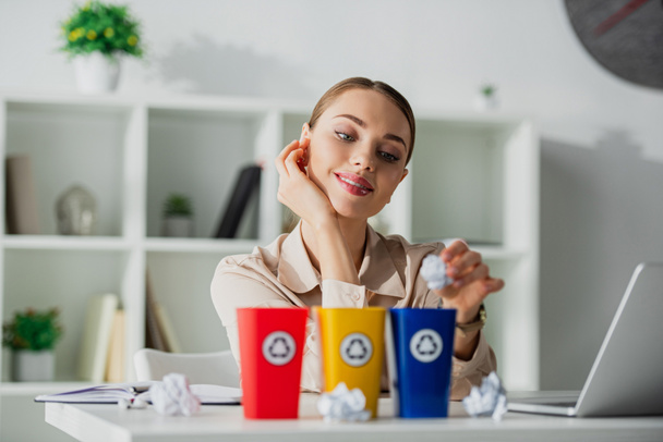 beautiful happy businesswoman throwing crumpled papers into recycling buckets  in office  - Photo, Image