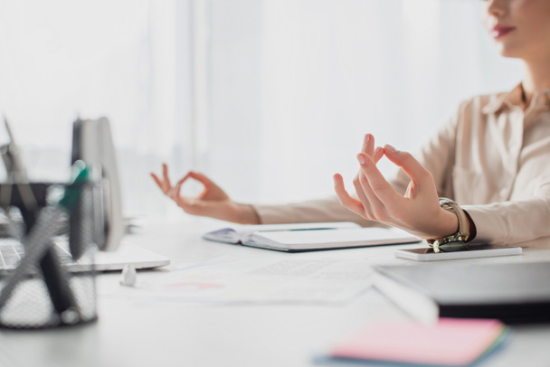 cropped view of businesswoman meditating with gyan mudra at workplace with notepad  - Fotoğraf, Görsel