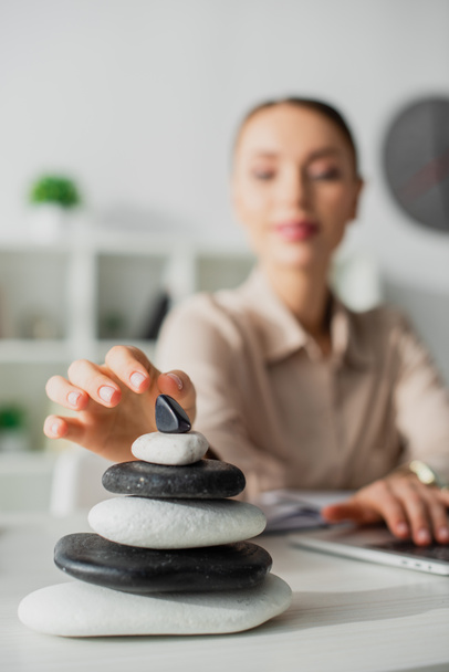 selective focus of businesswoman working with laptop at workplace with zen stones - Photo, Image