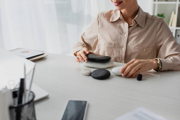 Ausgeschnittene Ansicht einer Geschäftsfrau am Arbeitsplatz mit Zen-Steinen, Smartphone und Laptop  - Foto, Bild