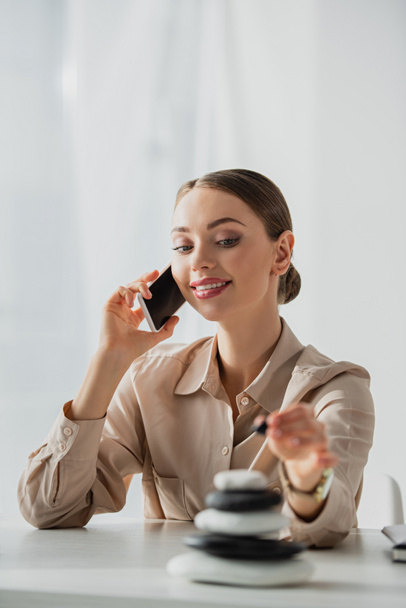 mulher de negócios feliz falando no smartphone no local de trabalho com pedras zen
 - Foto, Imagem