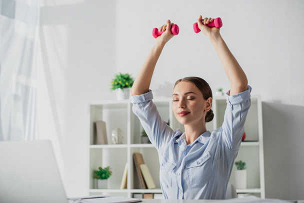 beautiful happy businesswoman with closed eyes training with dumbbells in office - Fotografie, Obrázek
