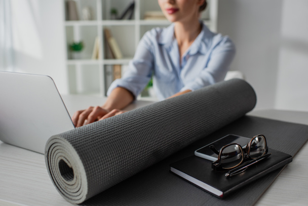 foyer sélectif de la jeune femme d'affaires travaillant sur ordinateur portable sur le lieu de travail avec tapis de yoga, bloc-notes, smartphone et lunettes
 - Photo, image