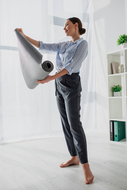 красива усміхнена молода бізнес-леді тримає йога килимок в офісі
 - Фото, зображення