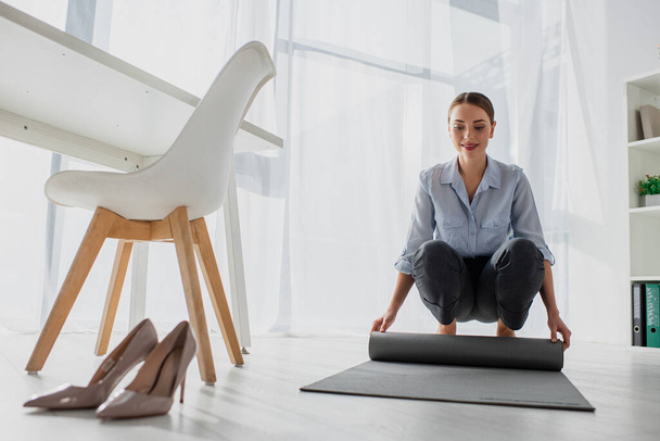 счастливая молодая предпринимательница кладет коврик для йоги на пол в офисе
 - Фото, изображение
