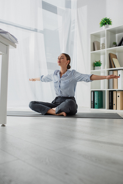 joven empresaria practicando yoga en posición de loto sobre estera en oficina
  - Foto, Imagen