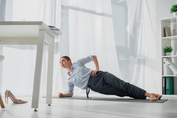 mosolygó üzletasszony gyakorló jóga oldalsó deszka szőnyeg az irodában  - Fotó, kép