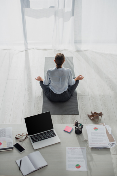 vista posteriore della donna d'affari che pratica yoga in posizione di loto con mudra gyan sul tappeto in ufficio
  - Foto, immagini