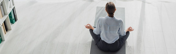 tiro panorâmico de empresária praticando ioga na posição de lótus com mudra gyan no tapete no escritório
  - Foto, Imagem