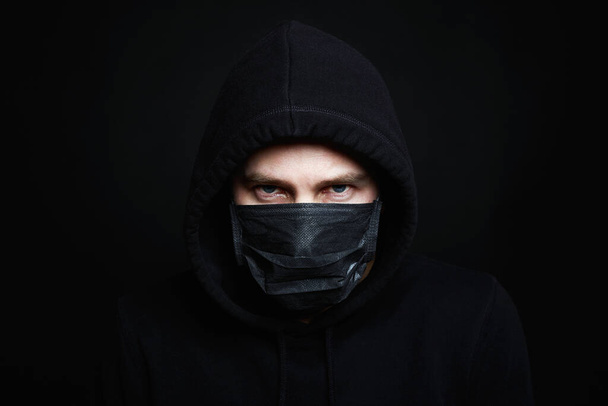 Man met masker en kap. Jongen in Black Mask en Hoodie. Coronavirusepidemie - Foto, afbeelding