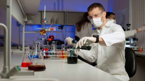 Científico joven mezclando líquidos de colores en un frasco
. - Foto, Imagen