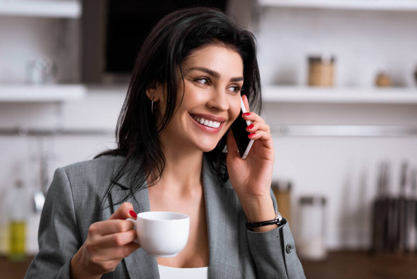 happy businesswoman holding cup of coffee and talking on smartphone while hiding problem of domestic violence  - Photo, Image