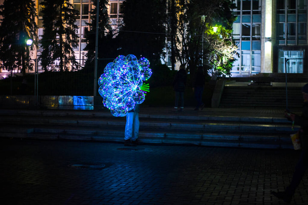 A man holding illuminating balloons with led garland in the street during the night. - Photo, Image