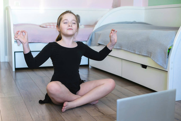 Школярка дивиться онлайн відео на ноутбук і займається спортом - йога, гімнастика, хореографія. Залишайся вдома. Концепція самоізоляції, карантину, онлайн-освіти
. - Фото, зображення