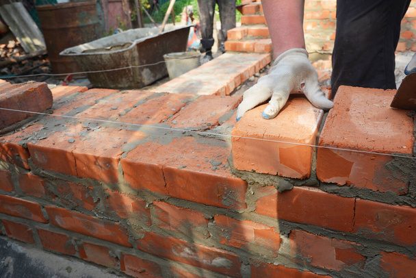 Egy kőműves vagy kőműves vörös téglákat fektet cementtel, hogy megépítse a ház falát.. - Fotó, kép