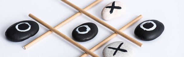 panoramic shot of tic tac toe game with grid made of paper tubes, and pebbles marked with naughts and crosses on white surface - Photo, Image
