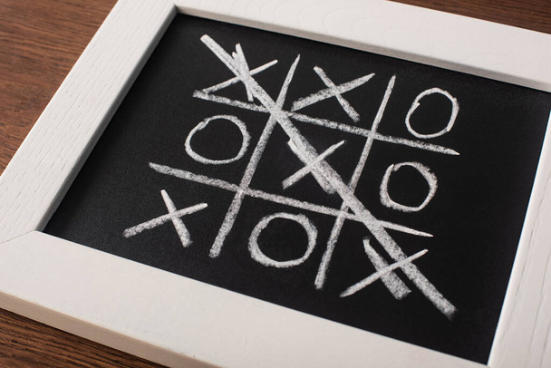 tic tac toe game on blackboard with crossed out row of crosses on wooden surface - Foto, afbeelding
