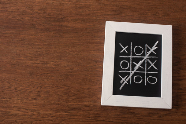 bovenaanzicht van tic tac toe spel op schoolbord met doorgestreepte rij kruisen op houten oppervlak - Foto, afbeelding