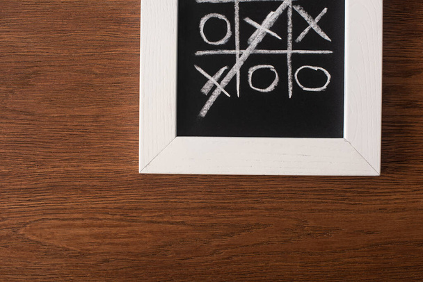 bovenaanzicht van tic tac toe spel op schoolbord met doorgestreepte rij kruisen op houten oppervlak - Foto, afbeelding