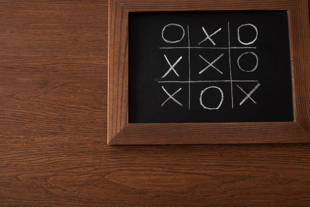 bovenaanzicht van tic tac toe spel op schoolbord met krijt rooster, naughts en kruisen op houten oppervlak - Foto, afbeelding