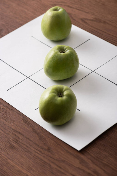 tic tac toe gra na białym papierze z rzędu trzech zielonych jabłek na drewnianej powierzchni - Zdjęcie, obraz