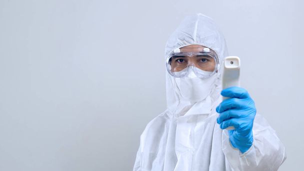 赤外線温度計、 IRサーモカン、保護PPEスーツを身に着けている顔マスクと眼鏡でアジアの医師を自信を持ってスキャン医療従事者 - 写真・画像