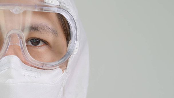 Close up open eye of Asian doctor in protective hazmat PPE suit wearing face mask and eyeglasses with copy space - Photo, Image