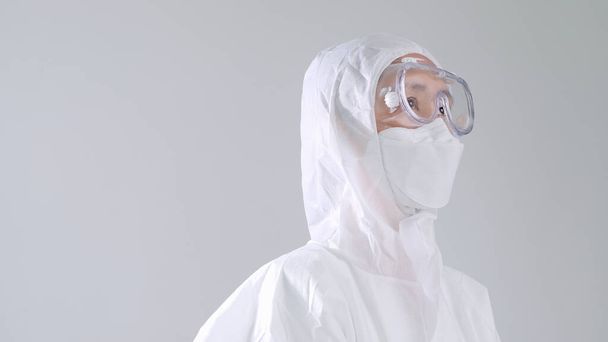 Азиатский врач в защитном защитном костюме СИЗ в маске и очках, смотрящий вверх с копировальным пространством - Фото, изображение