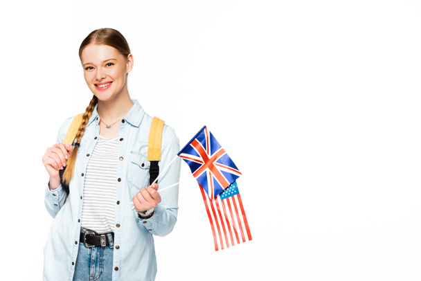 щаслива дівчина з тасьмою і рюкзаком тримає прапори Америки і об'єднане королівство ізольовано на білому
 - Фото, зображення