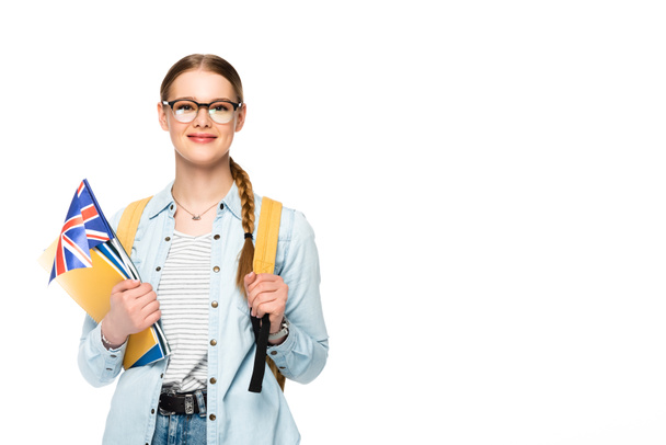 smiling girl in glasses with braid and backpack holding flag of united kingdom and copybooks isolated on white - Photo, Image