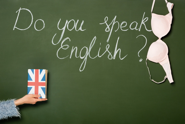 cropped view of girl holding book with uk flag near chalkboard with do you speak English lettering and bra - Foto, Imagem