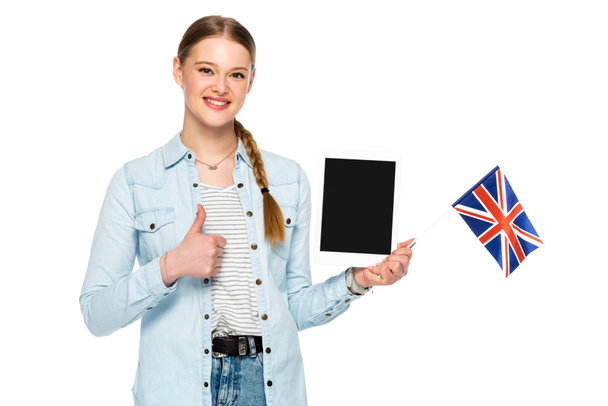lächelndes hübsches Mädchen mit Zopf, das ein digitales Tablet mit leerem Bildschirm und UK-Flagge hält, während es den Daumen nach oben zeigt, isoliert auf Weiß - Foto, Bild