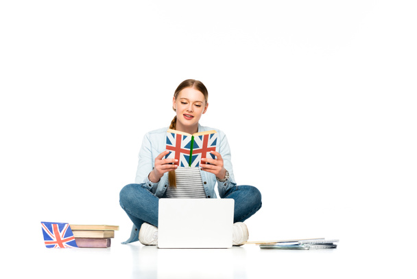 chica sentada en el suelo con el ordenador portátil, copybooks y bandera del Reino Unido, mientras que la lectura de libro aislado en blanco
 - Foto, Imagen
