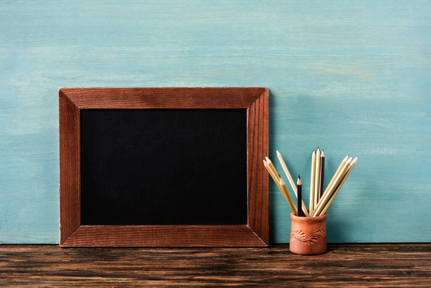 empty chalkboard near pencils on wooden table near blue wall - Fotografie, Obrázek