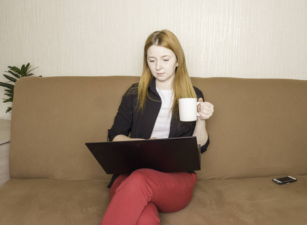 Kształcenie i praca online na odległość. Dziewczyna pracuje nad laptopem na kanapie. Praca zdalna. - Zdjęcie, obraz