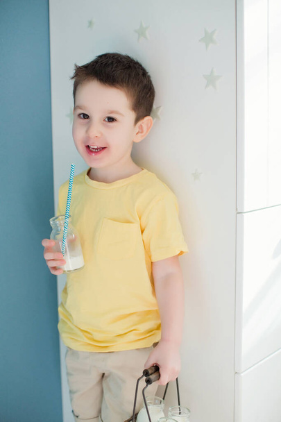 Enfant garçon caucasien dans un t-shirt jaune détient des bouteilles vintage avec du lait
 - Photo, image