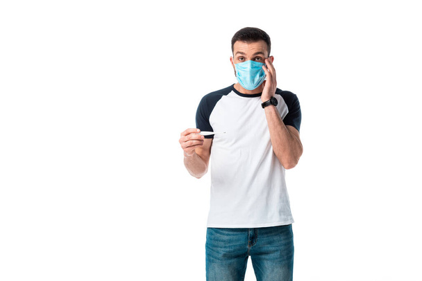 άρρωστος άνθρωπος με ιατρική μάσκα κρατώντας ψηφιακό θερμόμετρο απομονωμένο σε λευκό  - Φωτογραφία, εικόνα