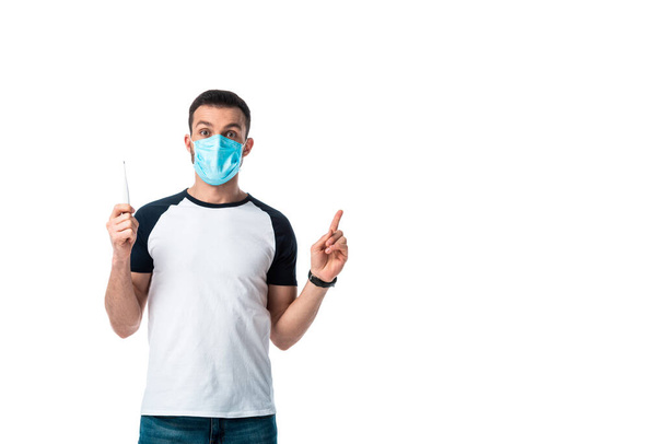 хворий чоловік у медичній масці тримає цифровий термометр і вказує пальцем ізольовано на білому
  - Фото, зображення