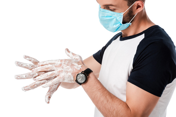 hombre en máscara médica mirando manos jabonosas aisladas en blanco
  - Foto, Imagen