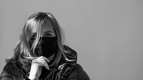 Menina, jovem mulher de máscara médica estéril protetora em seu rosto olhando para a câmera ao ar livre. Fotografia em preto e branco. Espaço de texto
. - Foto, Imagem