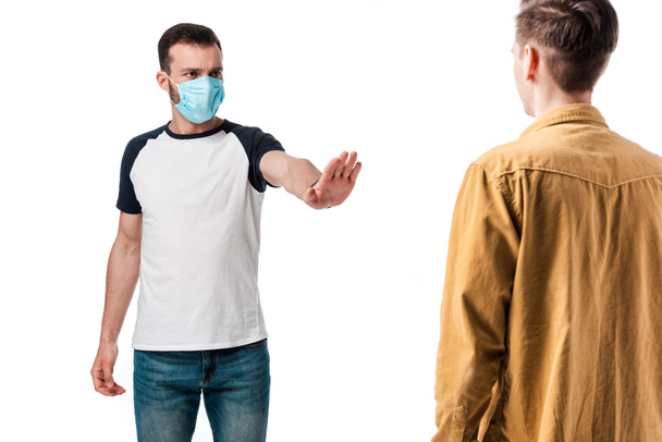 selective focus of man in medical mask showing stop gesture near guy isolated on white  - Photo, Image